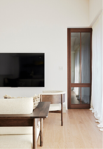 壁掛けテレビと木製建具のある明るいリビング