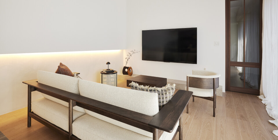 宿泊棟のリビング。ソファとローテーブル、壁掛けテレビが並び、木製建具の向こうに隣室がつながる家族団らんの空間。